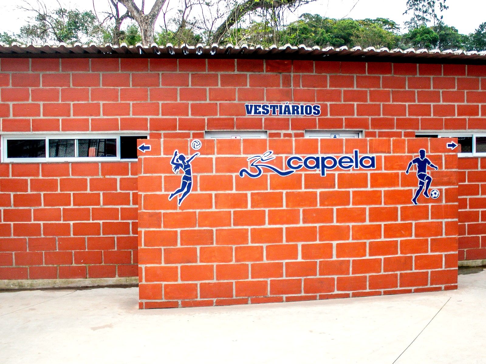 Fachada de tijolos dos vestiários, com a placa "Vestiários" e a marca Capela